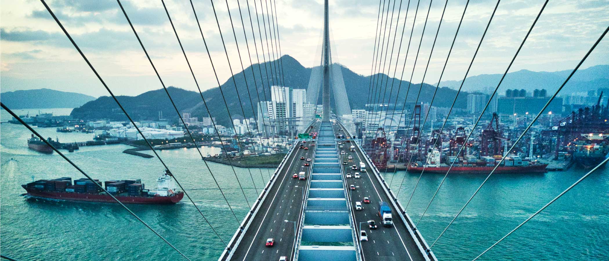 Large suspension bridge highway leading into a city, with a cargo ship passing below.