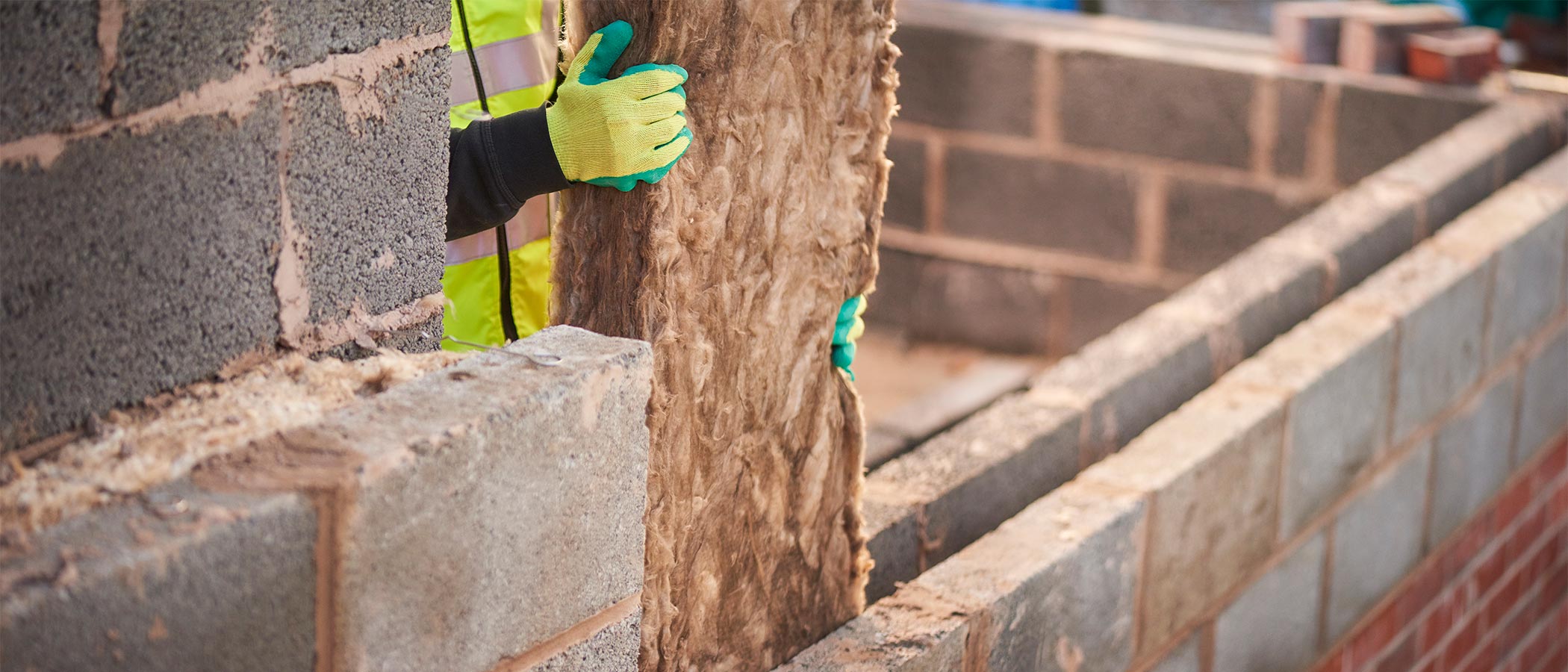 Worker installing cavity insulation between interior and exterior brick walls.